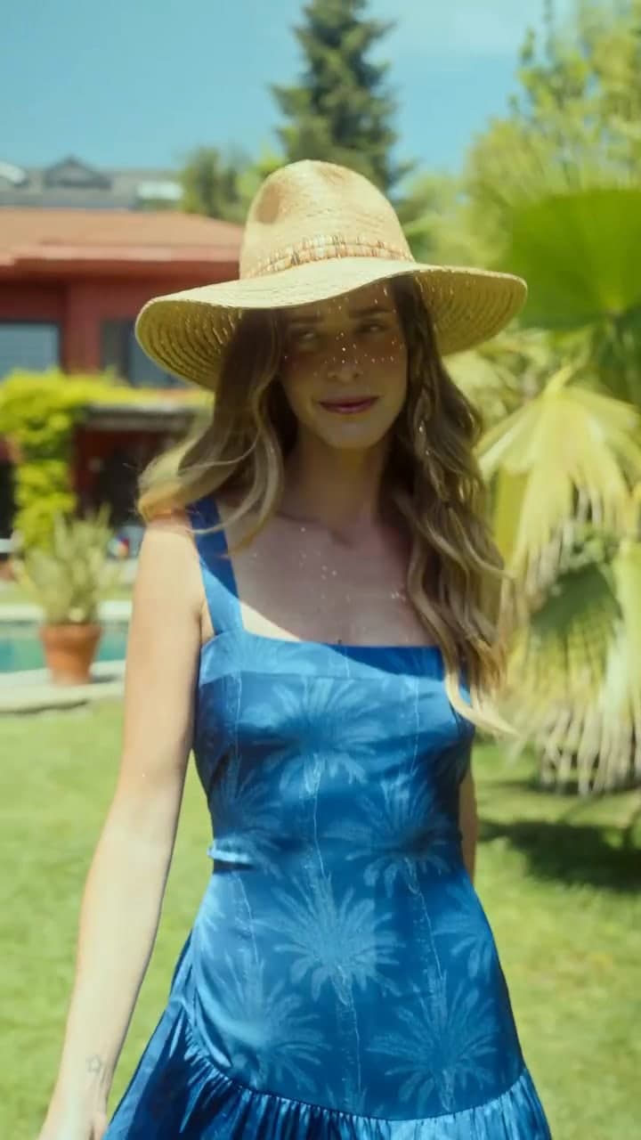A woman in a straw hat and a blue sundress in a green garden.